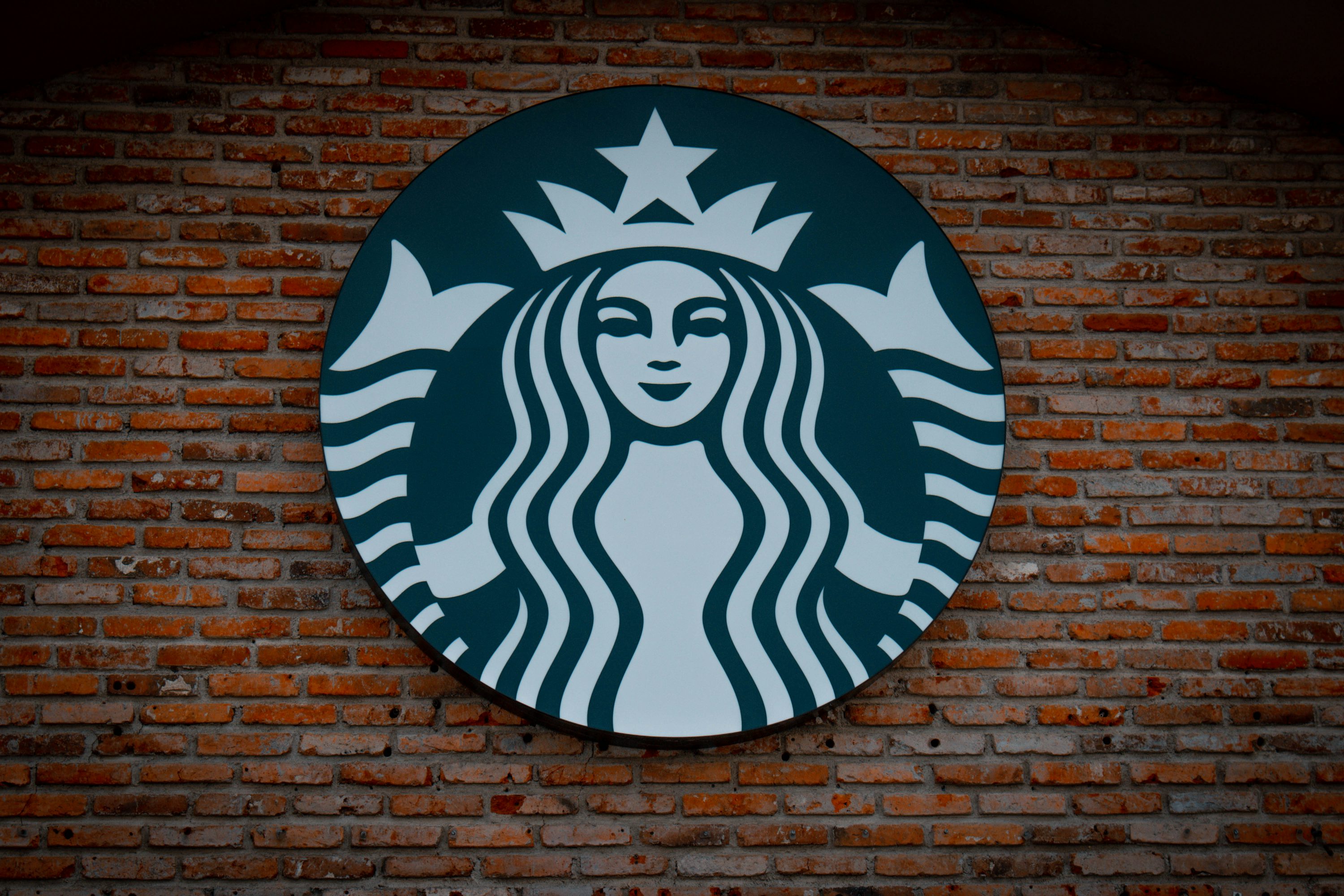 Logo zelené sirény Starbucks na cihlové zdi