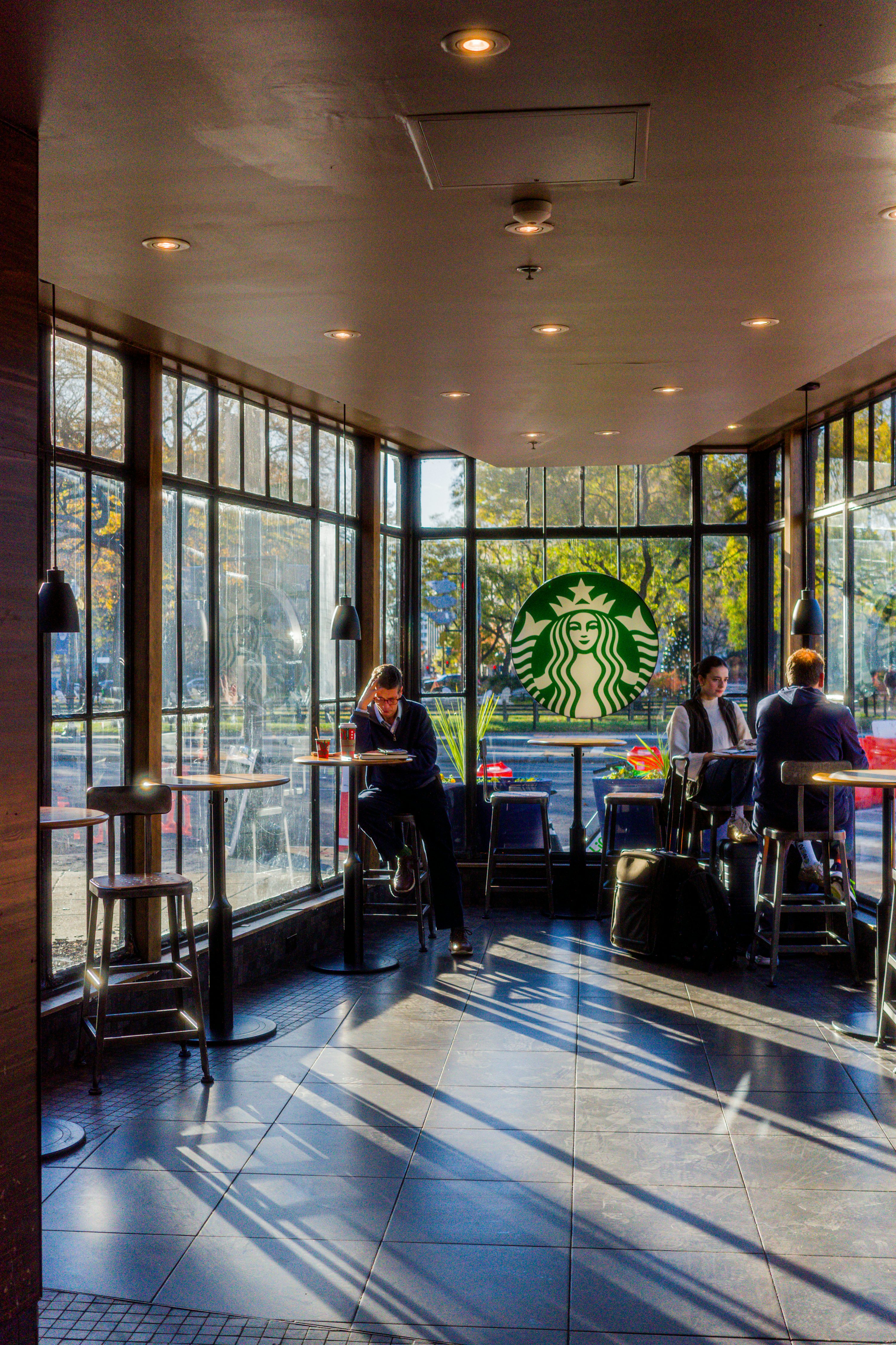 Interiér kavárny Starbucks s logem sirény na okně a hosty u stolků
